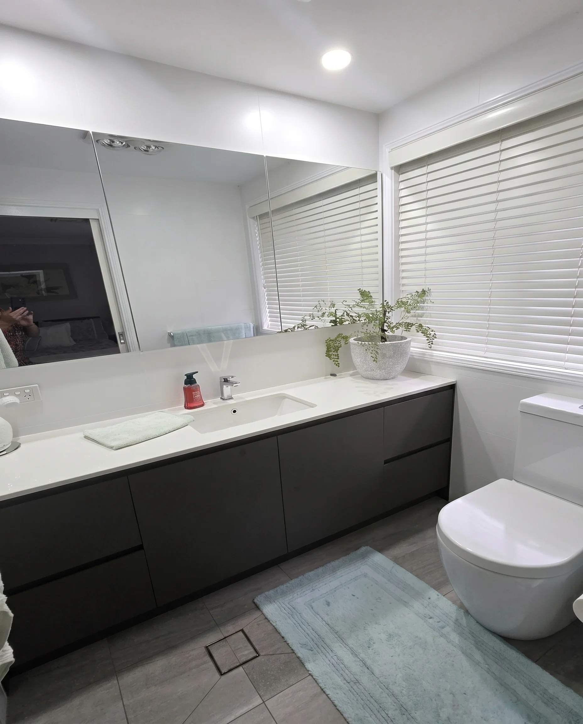 Dark floating vanity with white benchtop and large wall mirror