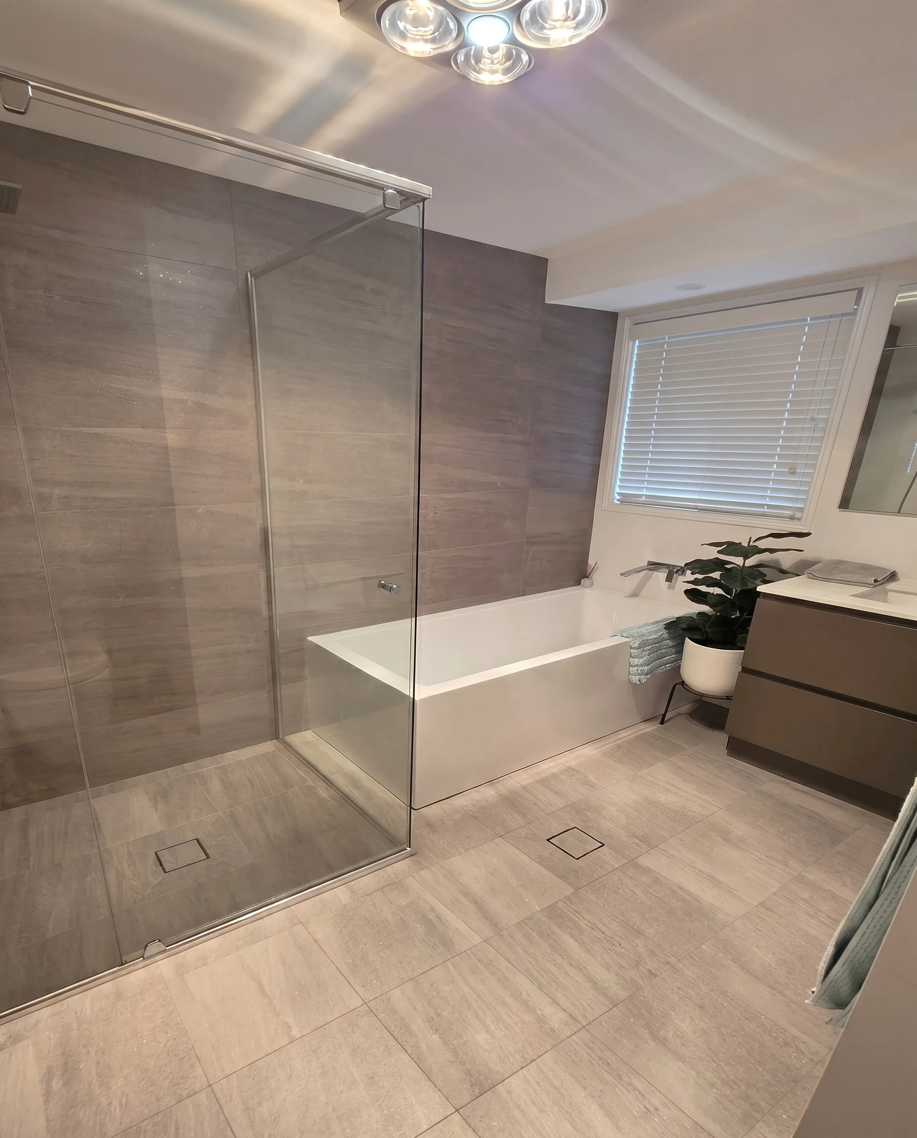 Full bathroom renovation with large format grey tiles, glass shower and freestanding bath