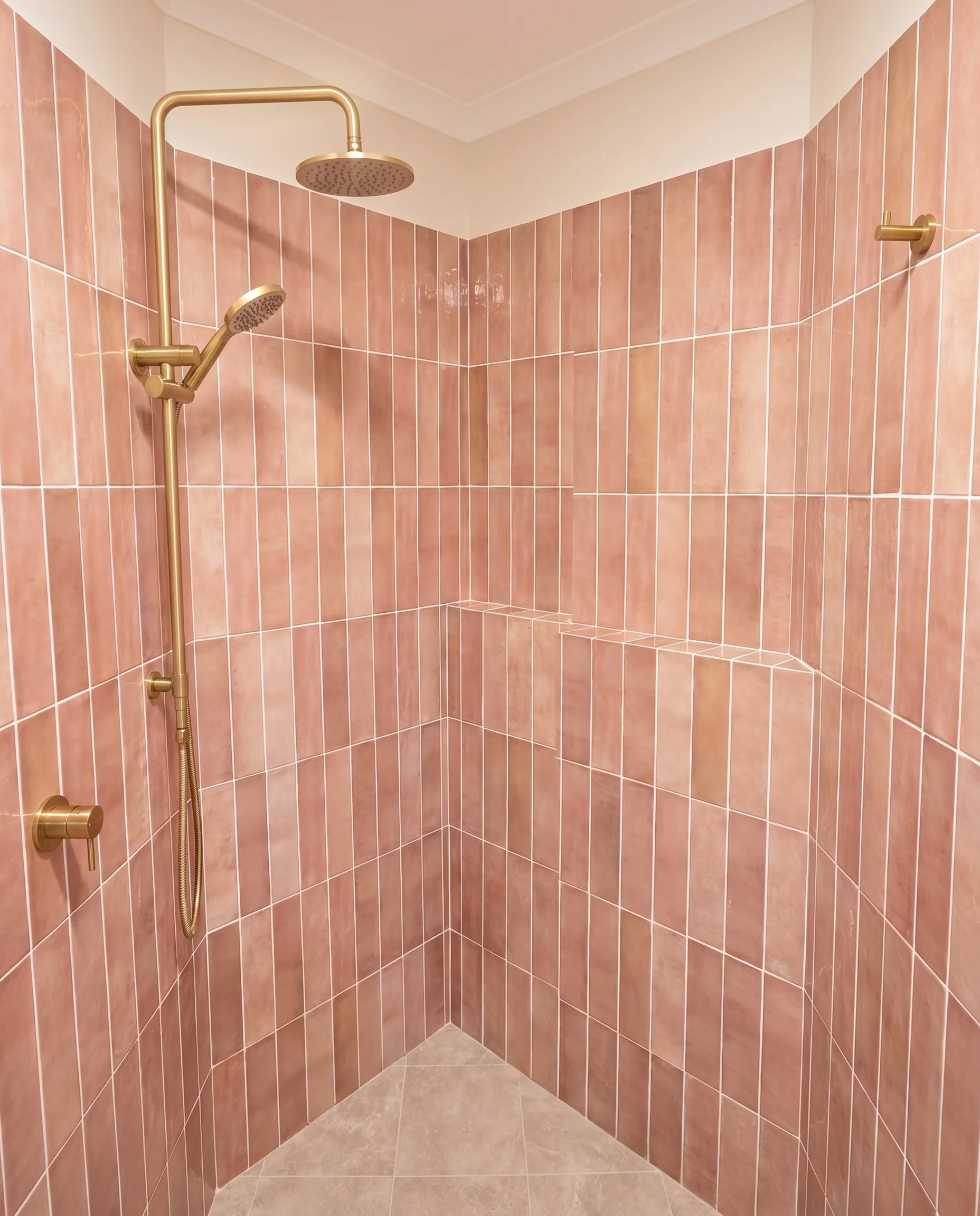 Pink terracotta shower tiles with brass shower column and rain head