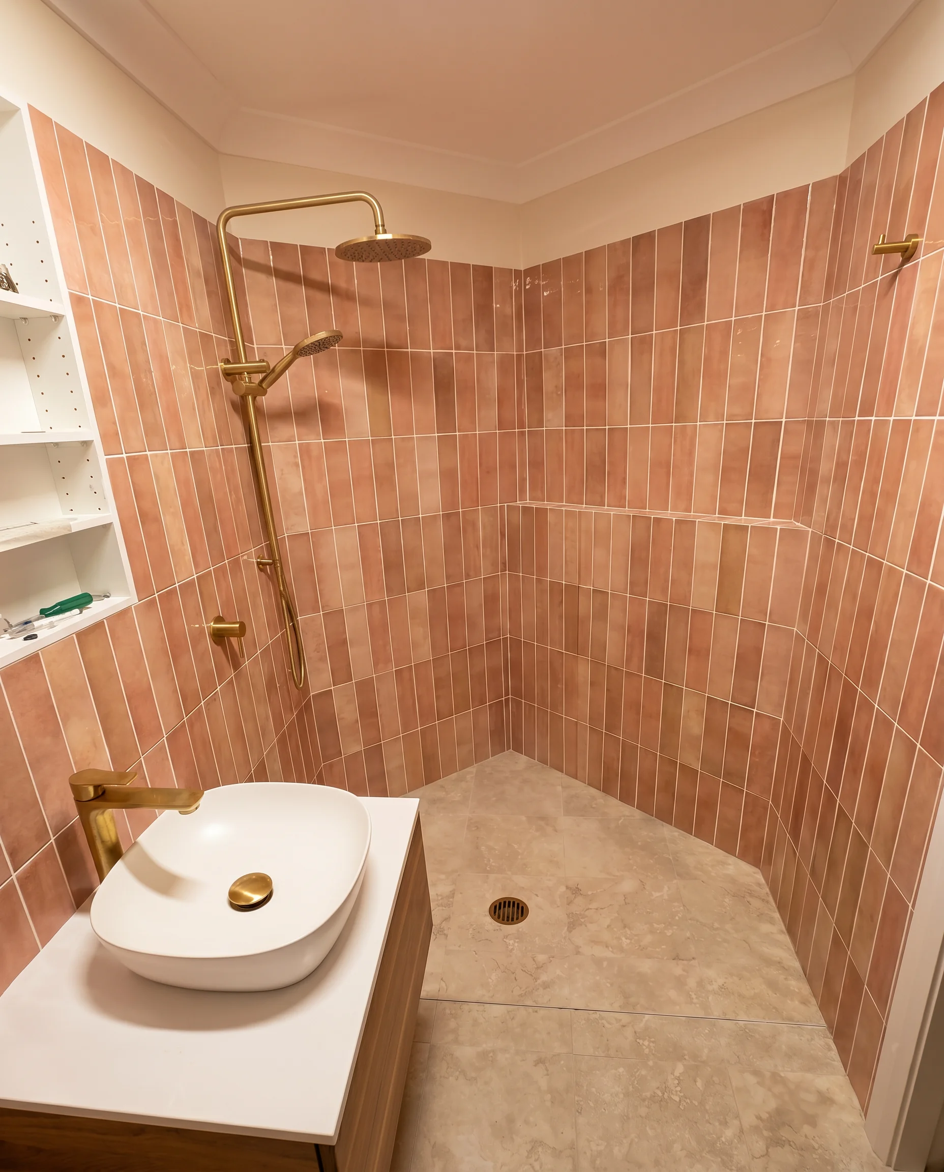 Pink terracotta wall tiles with brass tapware and floating timber vanity